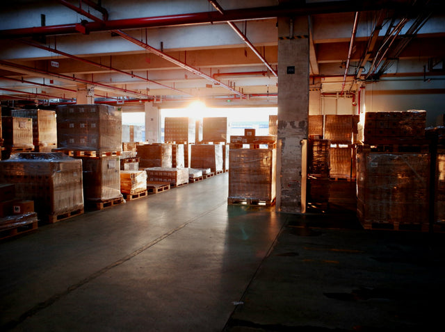Möbelqualität erkennen beginnt im Lager: Hallenlager mit verpackten Waren auf Paletten im Gegenlicht